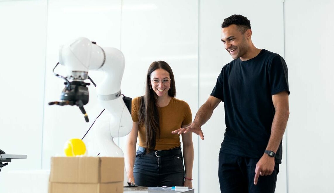 Two engineers collaborating on testing a futuristic robotic prototype in a modern indoor lab.