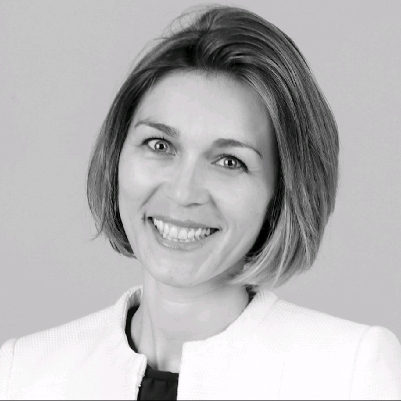 Portrait of a smiling professional woman with a short bob haircut, wearing a light blazer in grayscale.