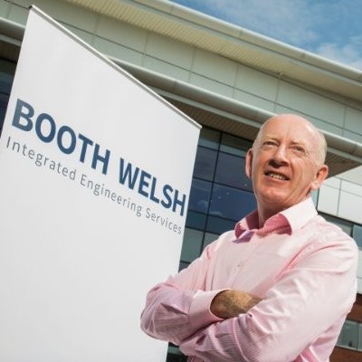 Martin Welsh - Industry 5.0 - Industry 5.0 Smiling man in a pink shirt stands beside a Booth Welsh banner reading 'Booth Welsh Integrated Engineering Services'.
